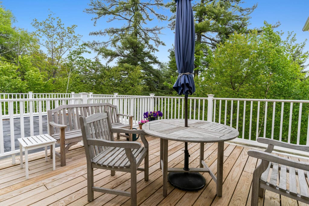 DSC01505-11209637 - Dirigo Pines A table and chairs sit outside on a porch surrounded with green trees and blue skies.