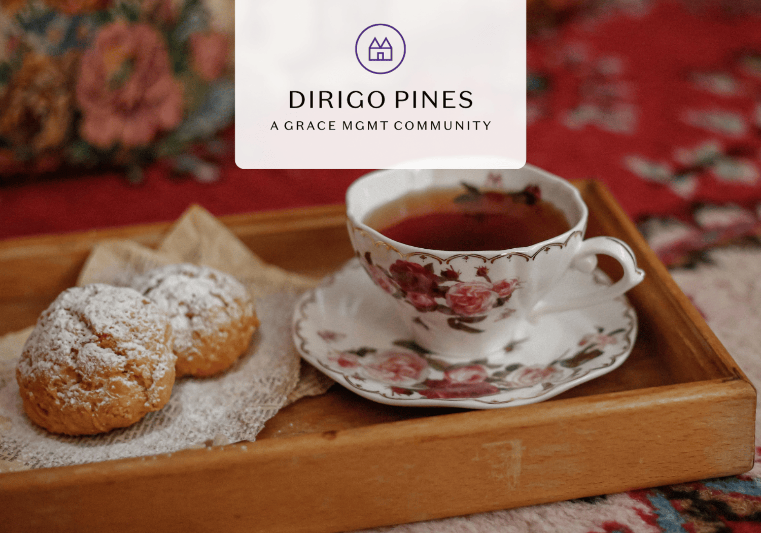 Tea cup with a floral pattern on a wooden tray, beside two powdered-sugar pastries on a napkin