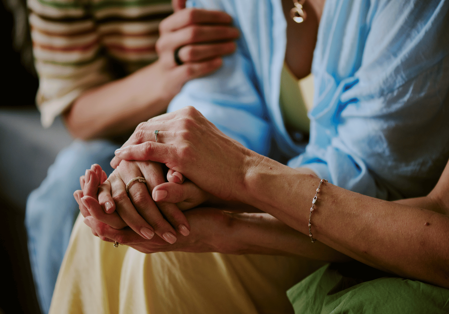 Two people hold hands in a comforting embrace, rings visible on their fingers.