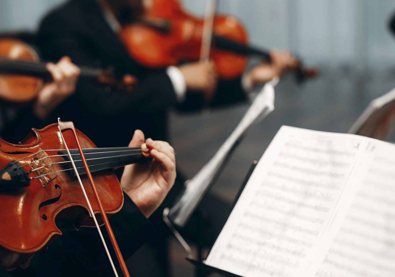 Close-up of a violinist's hand playing a violin, bow drawn across strings, with sheet music in the foreground.